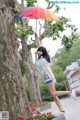 A woman standing next to a tree holding an umbrella.