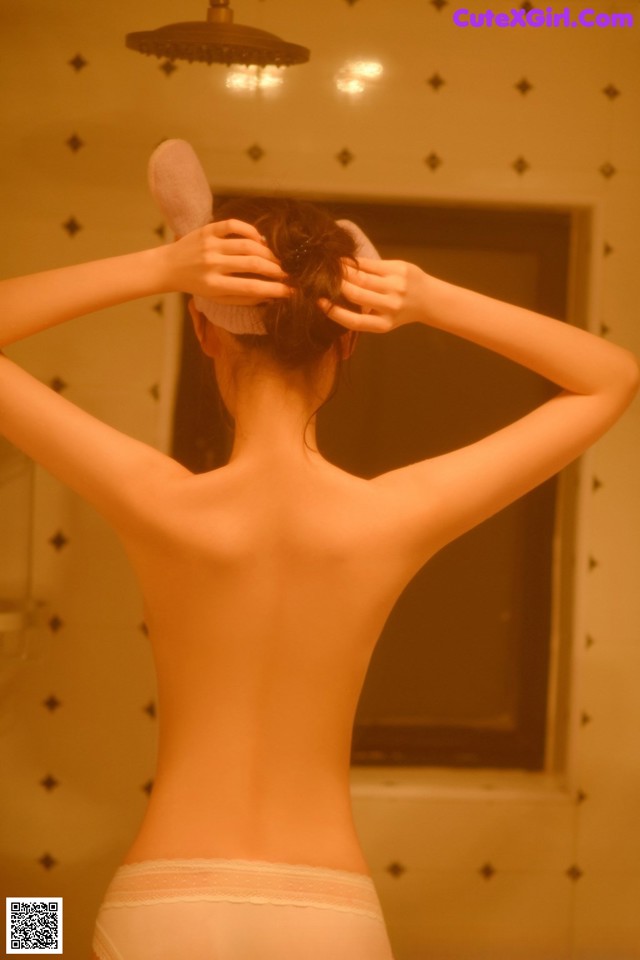 A woman in a white underwear brushing her hair in the bathroom.