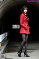 A woman in a red coat and black tights posing for a picture.