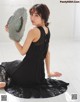 A woman in a black dress sitting on the floor holding a hat.