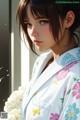 A woman in a white kimono standing next to a bunch of flowers.