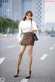 A woman in a white shirt and brown skirt is walking down the street.