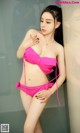 A woman in a pink bikini leaning against a wall.