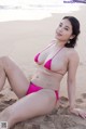 A woman in a pink bikini sitting on the beach.