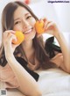 A woman laying on a bed holding two oranges.