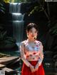 A woman in a red and white dress standing in front of a waterfall.