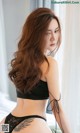 A woman in a black bra top and panties sitting on a bed.