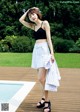 A woman standing next to a swimming pool wearing a black top and white skirt.