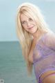 A woman in a purple lingerie posing by the ocean.