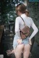 A woman in a white shirt and denim shorts holding a brown bag.