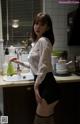 A woman in a white shirt and black skirt standing in a kitchen.