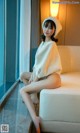 A woman sitting on a white couch wearing a white sweater.