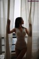 A woman in a white lingerie standing by a window.