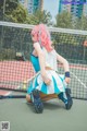 A woman with pink hair crouching on a tennis court.